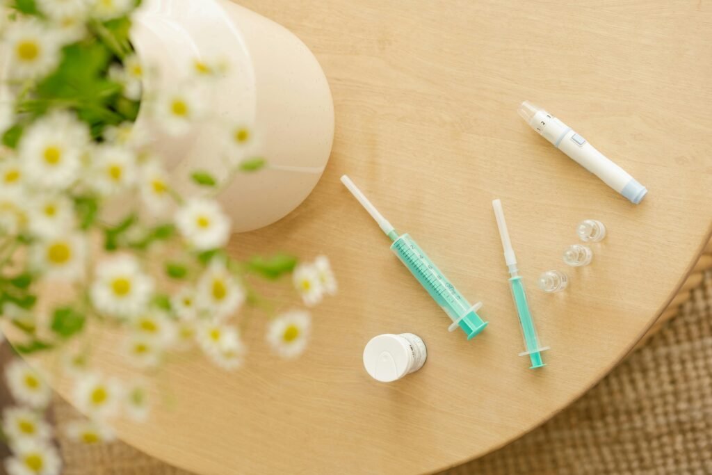 Top view of diabetic care kit with syringes and injector pen on a wooden table with flowers.